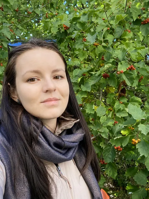 Анастасия на улице на фоне зелёных листьев